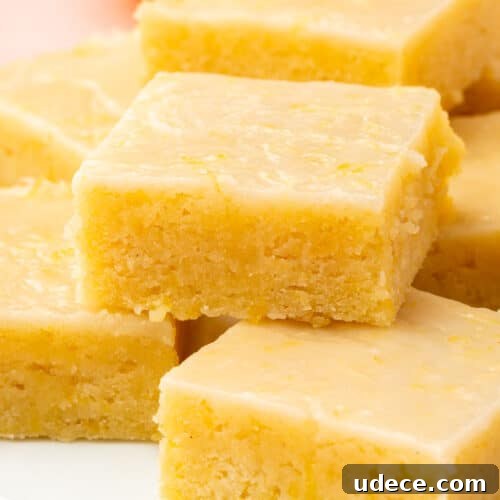 Gluten-Free Lemon Brownies Recipe — Zesty Citrus Brownie Bars 15 A stack of gluten free lemon brownies with lemon glaze on a white dessert plate.