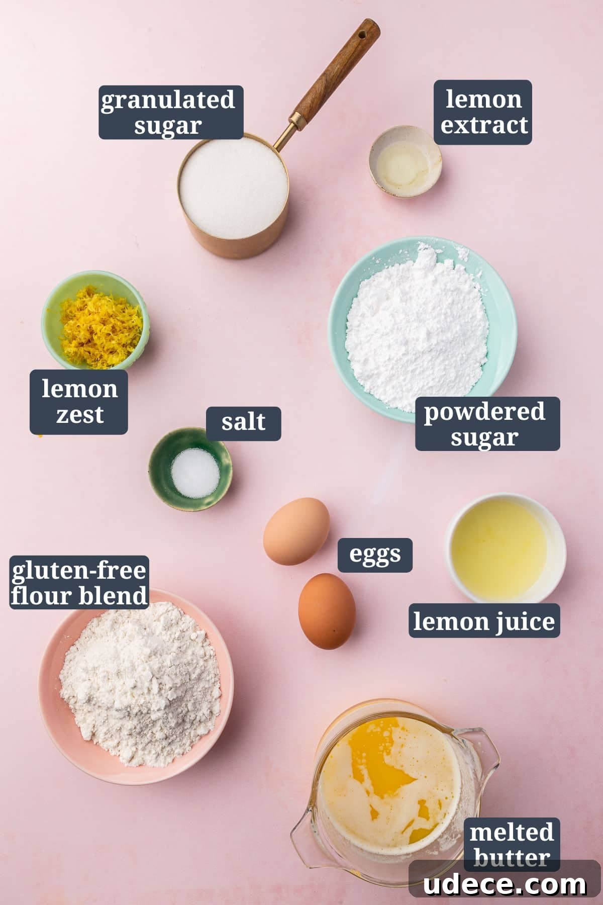 Gluten-Free Lemon Brownies Recipe — Zesty Citrus Brownie Bars 3 An overhead view of ingredients in bowls to make gluten free lemon brownies, including granulated sugar, lemon extract, lemon zest, salt, powdered sugar, eggs, lemon juice, gluten-free flour blend, and melted butter with text overlays over each ingredient.