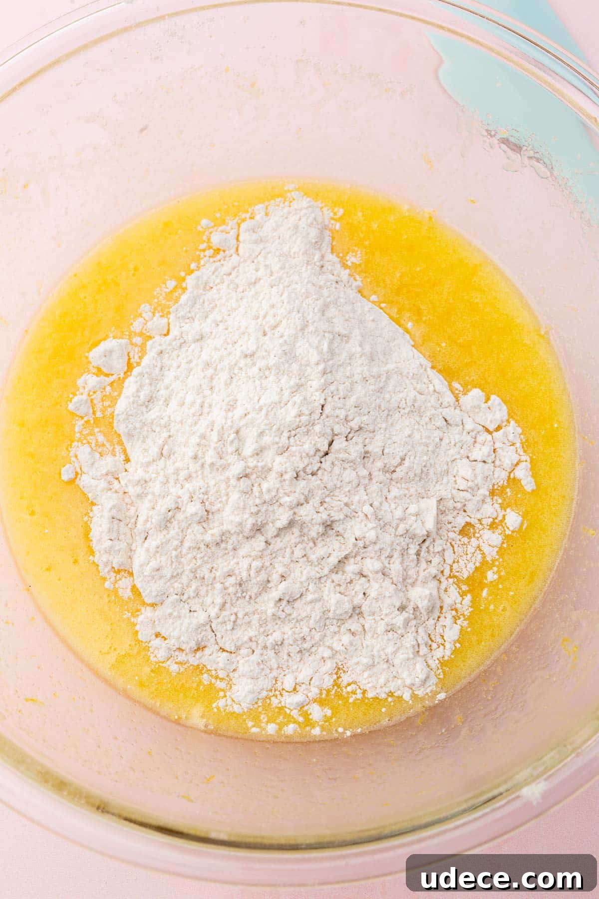 Gluten-Free Lemon Brownies Recipe — Zesty Citrus Brownie Bars 7 A glass mixing bowl with a lemon mixture topped with gluten-free flour before mixing together.