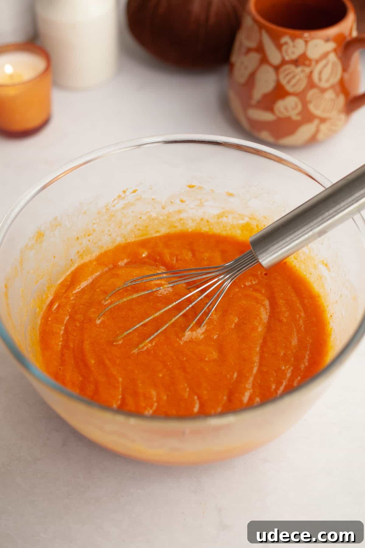 Pumpkin cake batter in a glass bowl with a whisk.