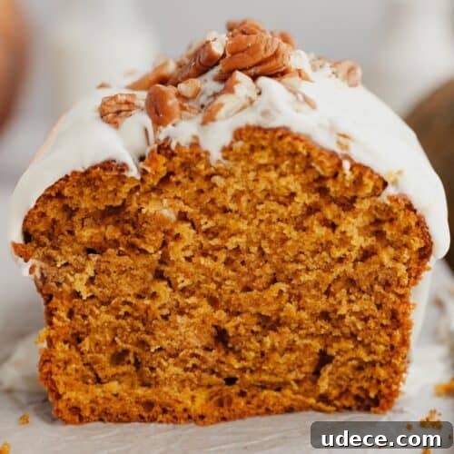 A slice of pumpkin bread with cream cheese frosting and chopped pecans on top.