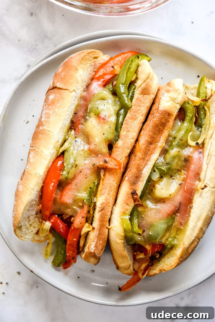 two air fryer sausage dogs with peppers and onions and melt cheese on a plate.