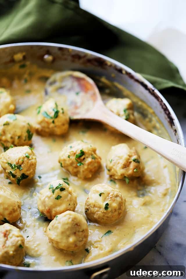 This baked turkey Swedish meatballs recipe with homemade mustard gravy is an easy twist on a classic comfort food. Angled photo of baked meatballs in the pan with gravy.