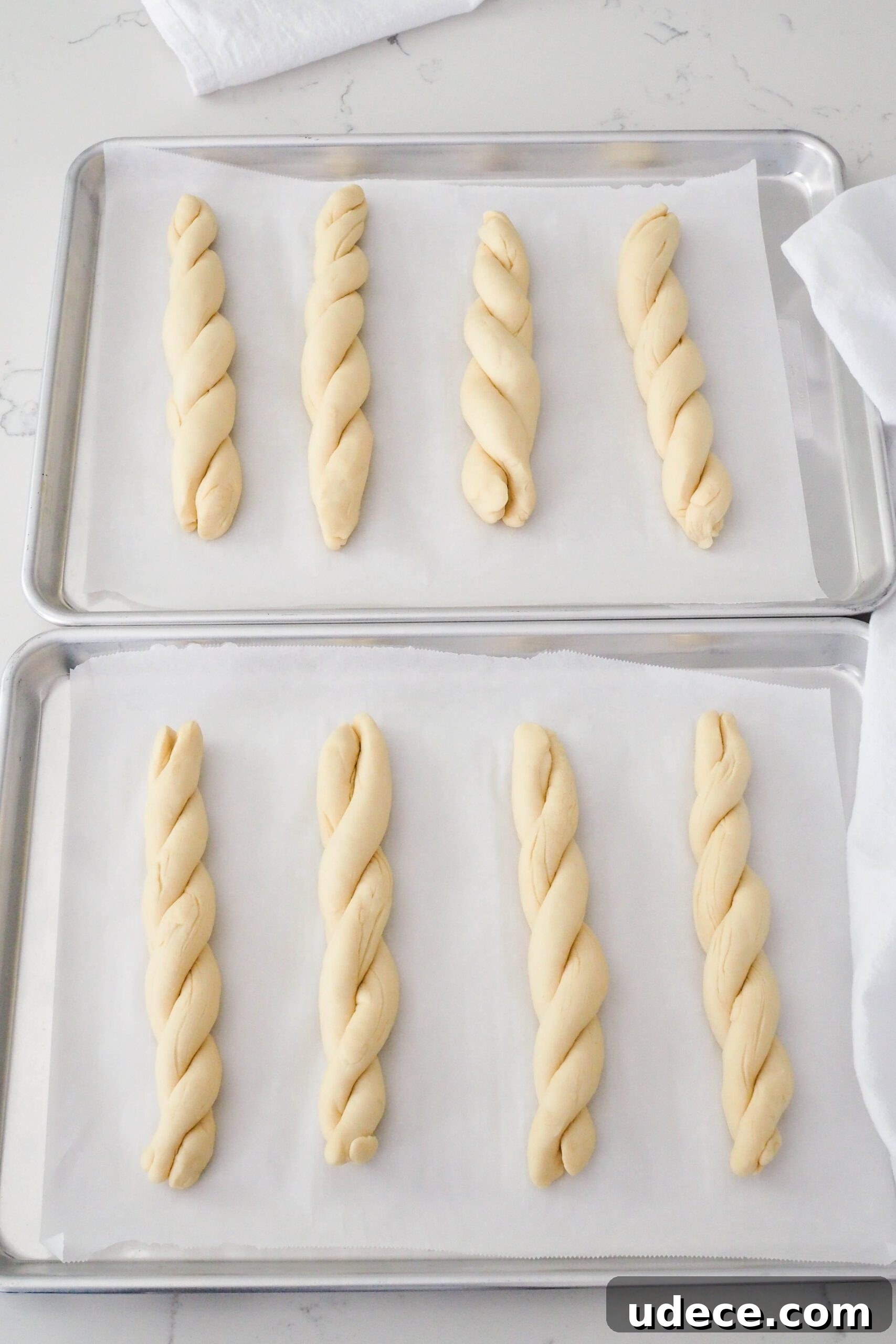 Crispy Homemade Garlic Breadsticks with Parmesan and Herbs 11 Eight proofed twisted garlic breadsticks on two baking sheets.