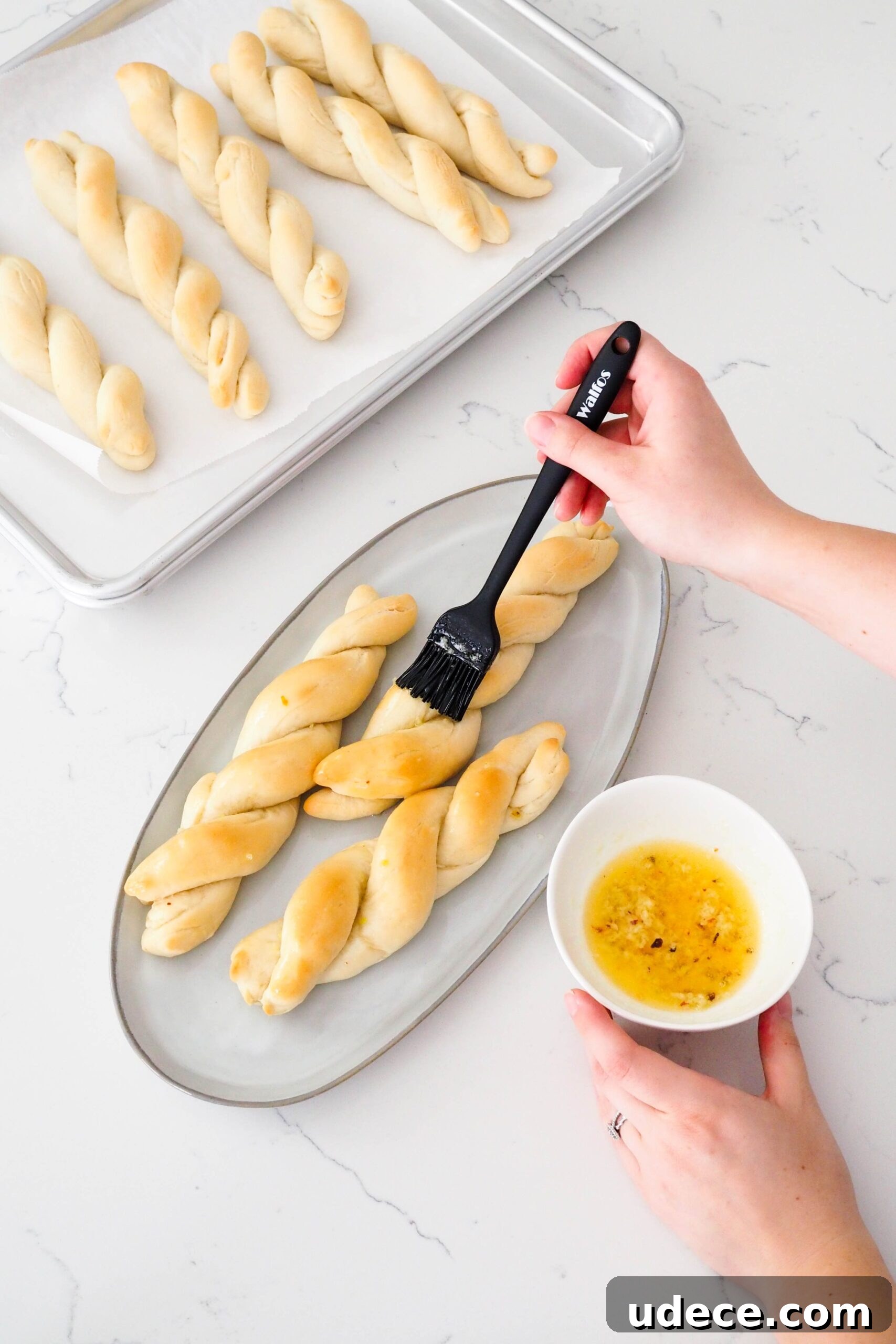 Crispy Homemade Garlic Breadsticks with Parmesan and Herbs 13 A hand brushes garlic butter onto three twisted garlic breadsticks.