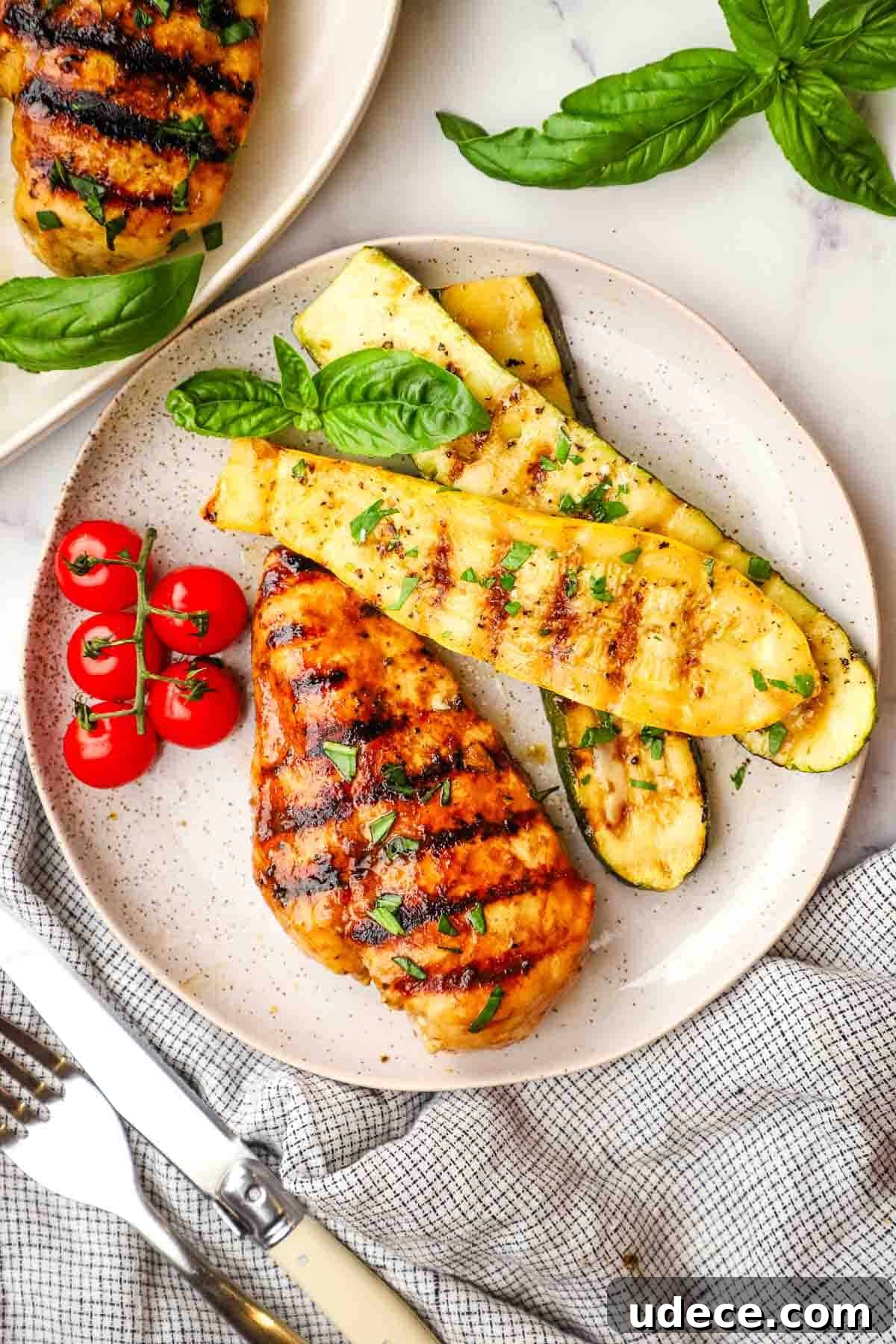 Grilled Balsamic Chicken with Garlic and Rosemary Marinade 2 A grilled chicken breast on a plate with grilled veggies and tomatoes.