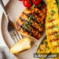 A grilled chicken breast on a plate with a bite on a fork.