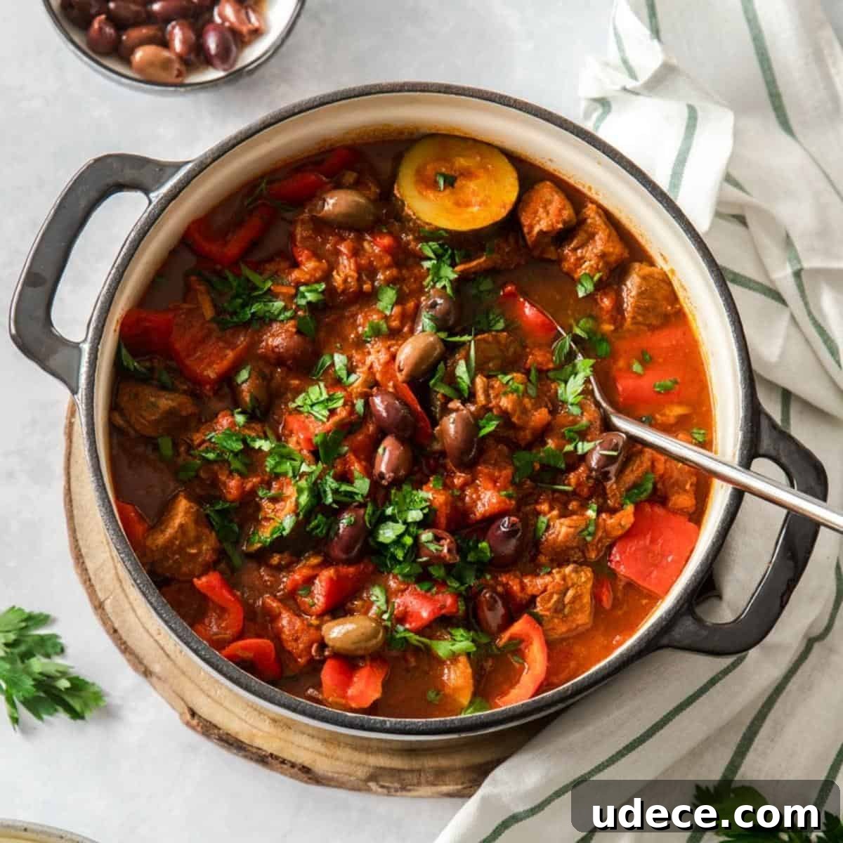 Dutch oven beef stew, with a silver serving spoon in dish which is garnished with parsley.