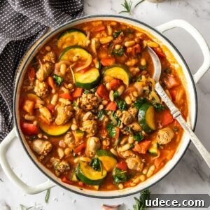 Mediterranean Sausage and Vegetable Casserole Recipe 13 Large saucepan of Sausage Casserole with a spoon in the pan, sitting on a marble bench top with some herbs around the edge.