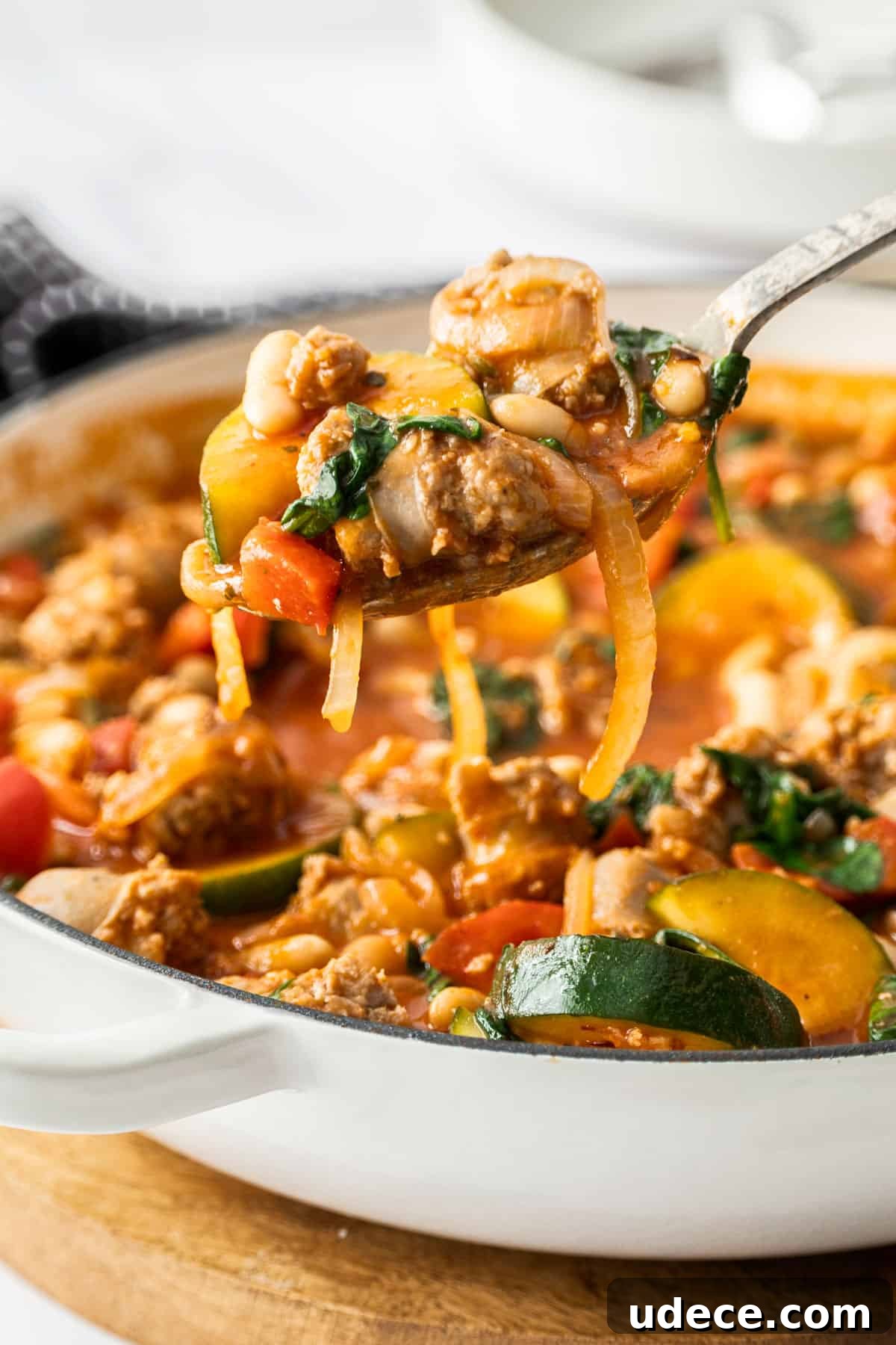 Mediterranean Sausage and Vegetable Casserole Recipe 8 Spoon lifting out some Sausage Casserole from a large white dish.