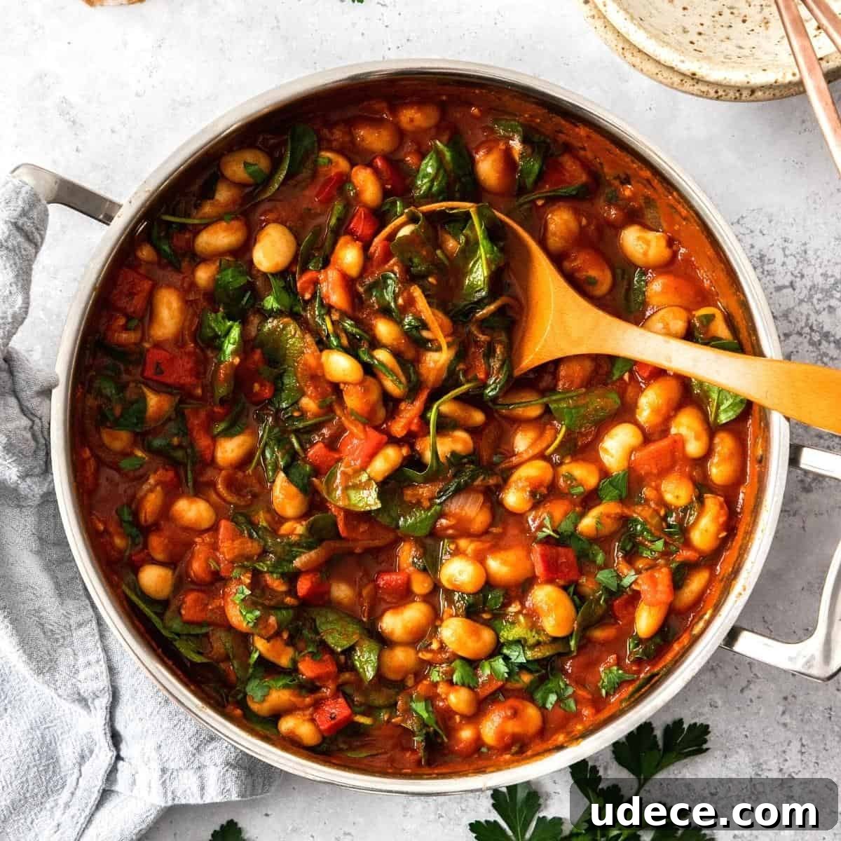 Round saucepan of butter bean stew, with a wooden spoon sitting in the pot.