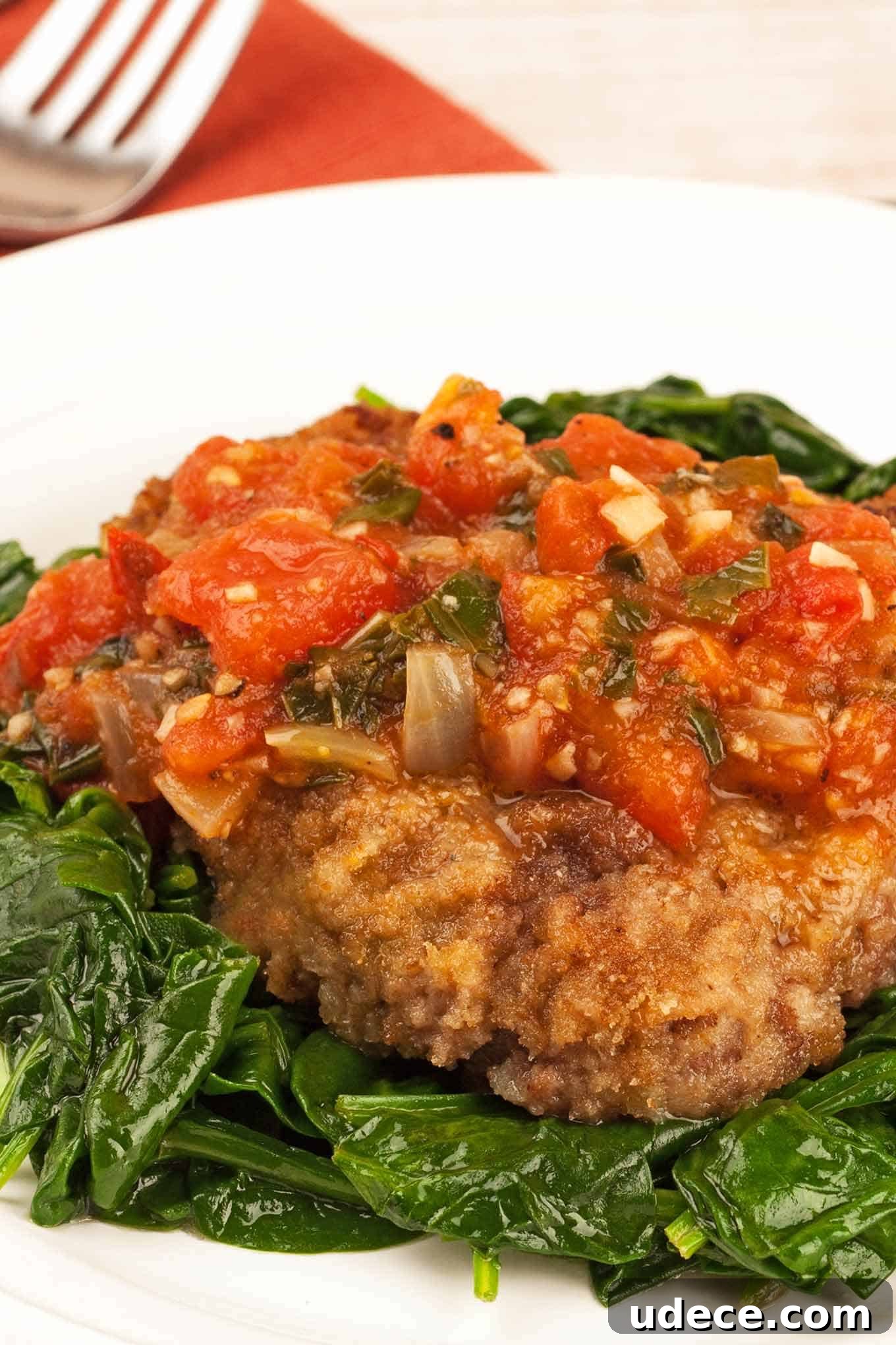 Milanese Steak: Crispy Breaded Veal-Style Cutlet Recipe 2 A plate of steak alla Milanese topped with tomato and herb sauce, served over a bed of sautéed spinach on a white plate.