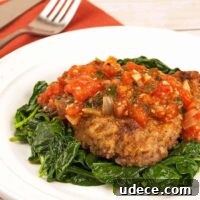 Milanese Steak: Crispy Breaded Veal-Style Cutlet Recipe 4 A plate of lightly breaded steak alla Milanese topped with tomato sauce, served over a bed of sautéed spinach.