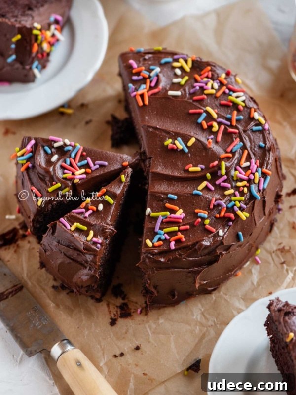 Moist Single-Layer Vanilla Bean Cake Recipe 8 Angled image of sliced single layer chocolate cake on parchment paper with slices of cake on small dessert plates around it and a knife on parchment paper.