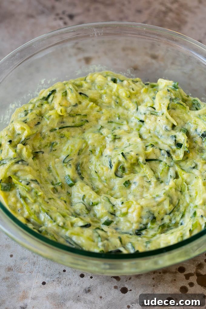 These zucchini fritters are crispy patties filled with shredded squash and flavored with garlic and herbs. Batter to make zucchini pancakes in a mixing bowl.