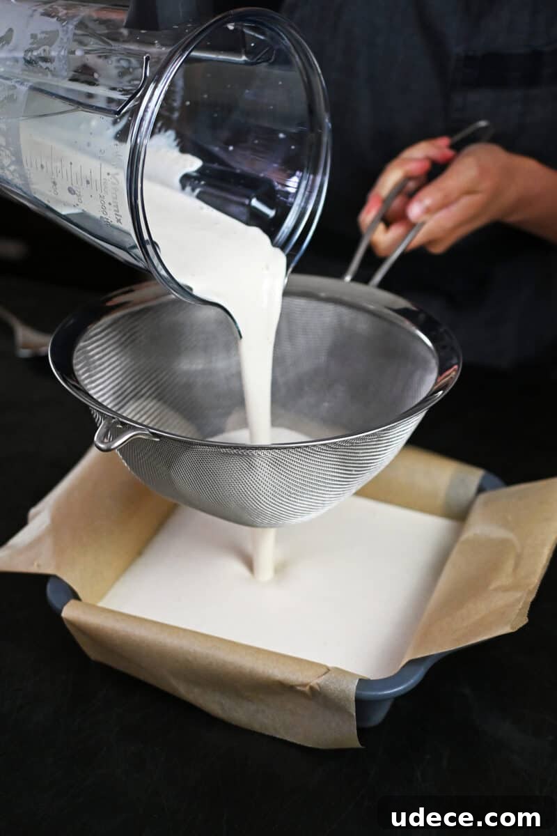 Vegan Coconut Cream Bars — Low-Carb, Gluten-Free Dessert 11 Pouring the coconut cream bar filling through a fine mesh sieve onto the crust in a square pan.
