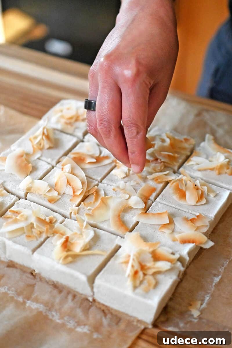 Vegan Coconut Cream Bars — Low-Carb, Gluten-Free Dessert 14 A hand adding toasted coconut flakes to squares of coconut cream bars.