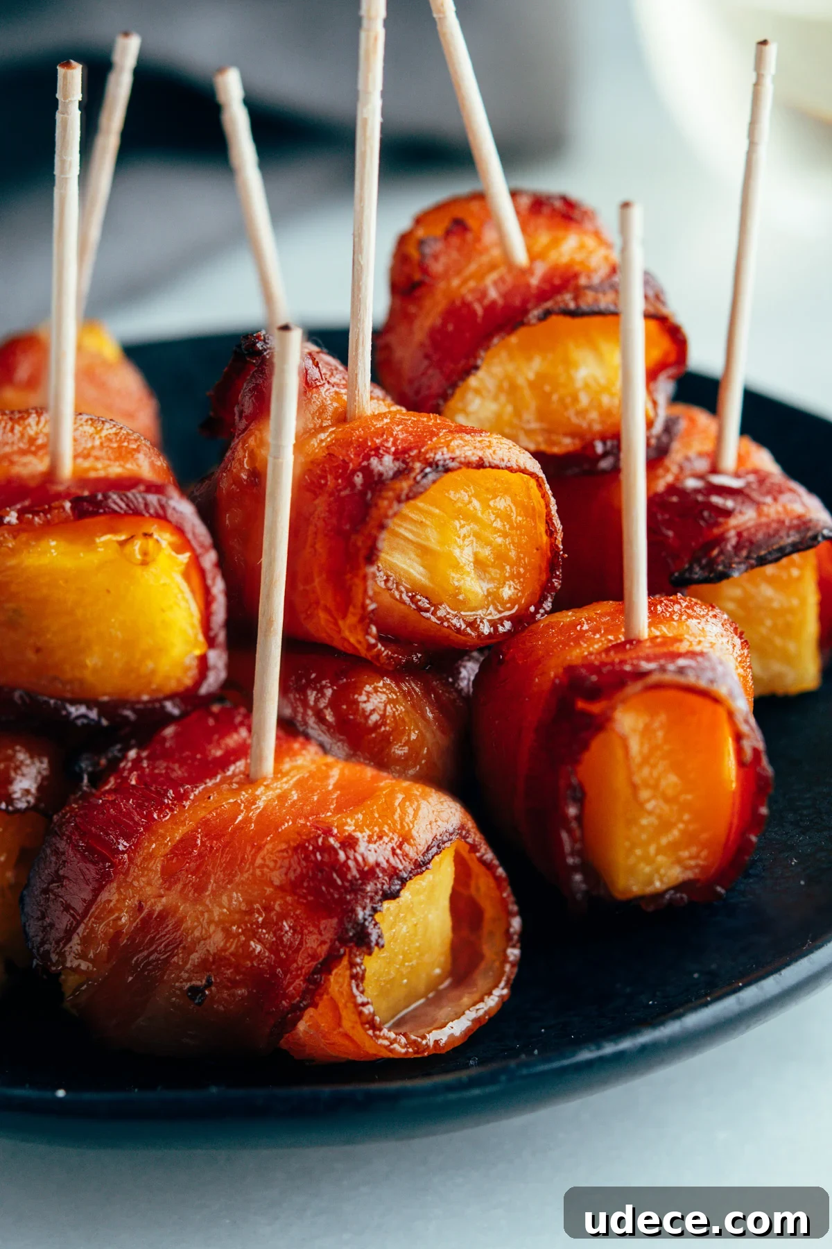 Crispy Bacon-Wrapped Pineapple Bites: Sweet and Savory Appetizer 2 Bacon Wrapped Pineapple served on a black plate.