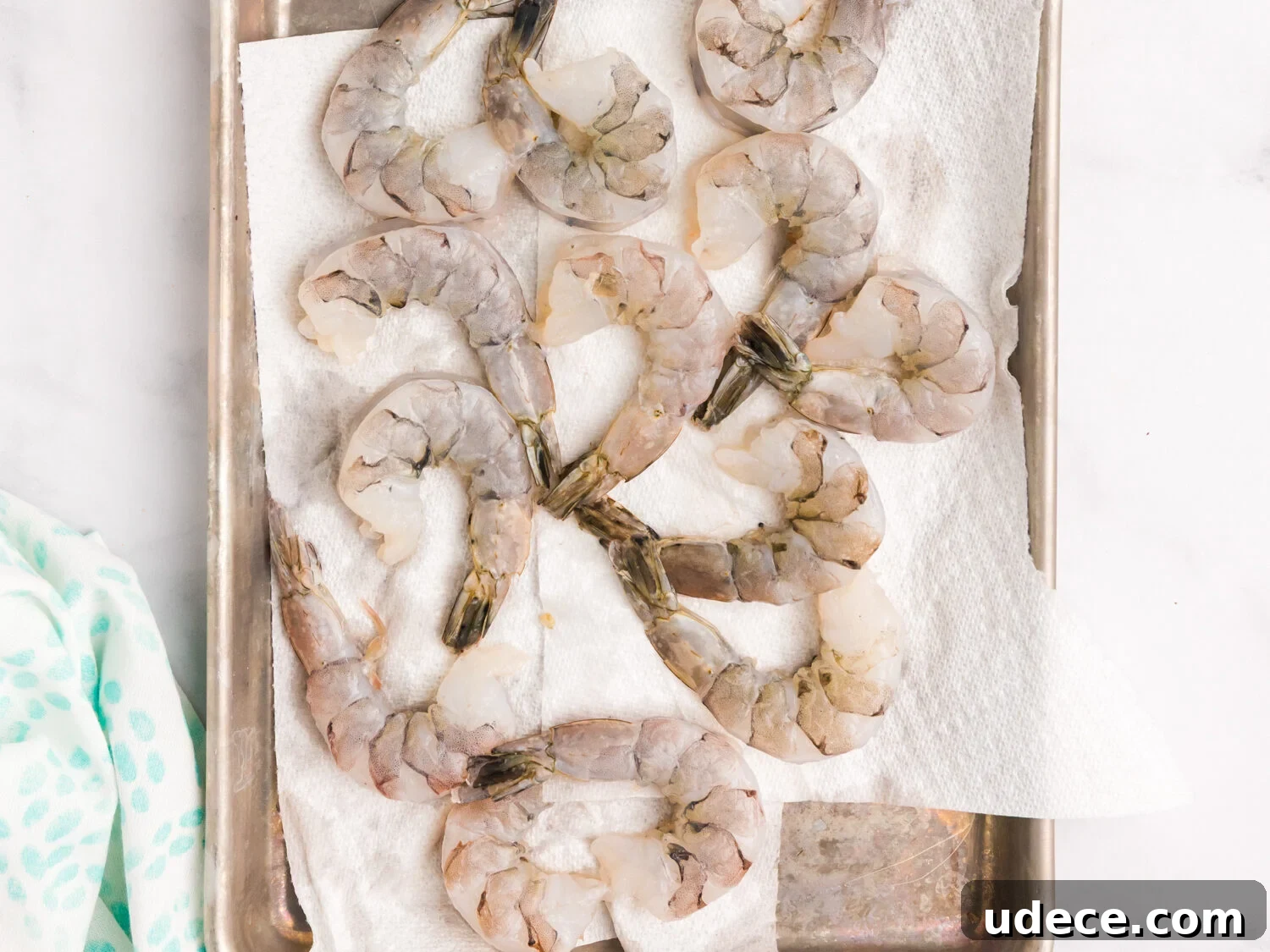 Spicy Cajun Grilled Shrimp Recipe for Quick Weeknight Meals 4 Raw, peeled shrimp laid out on a metal tray lined with paper towels, surrounded by lemon wedges, olive oil, seasoning mix, and salt and pepper shakers.