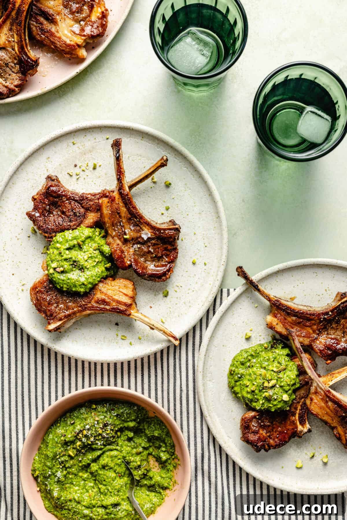 Grilled Lamb Chops with Fresh Arugula Pesto Recipe 2 White plates with grilled lamb chops and a dollop of arugula-pistachio pesto on a green and striped background
