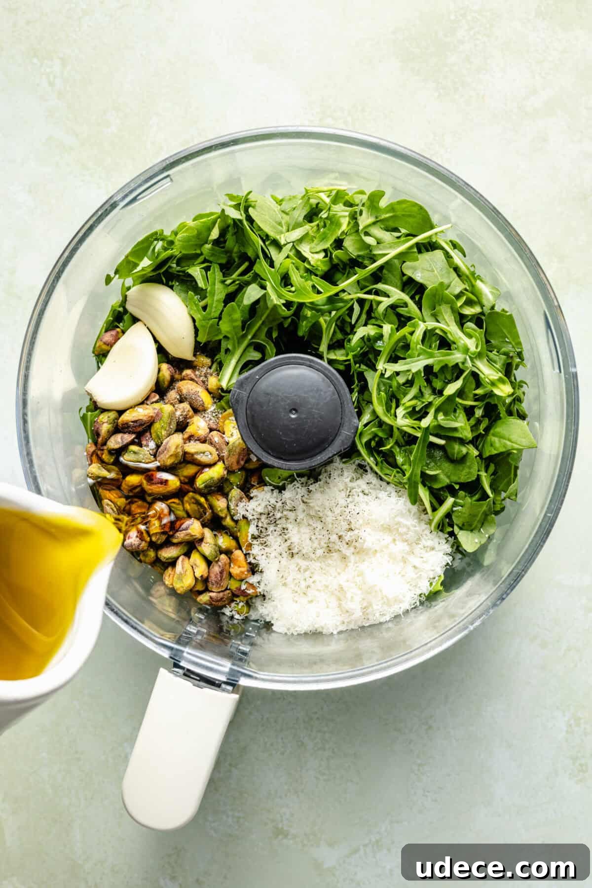 Grilled Lamb Chops with Fresh Arugula Pesto Recipe 3 a bowl of a food processor filled with arugula, pistachios, garlic, and parmesan cheese