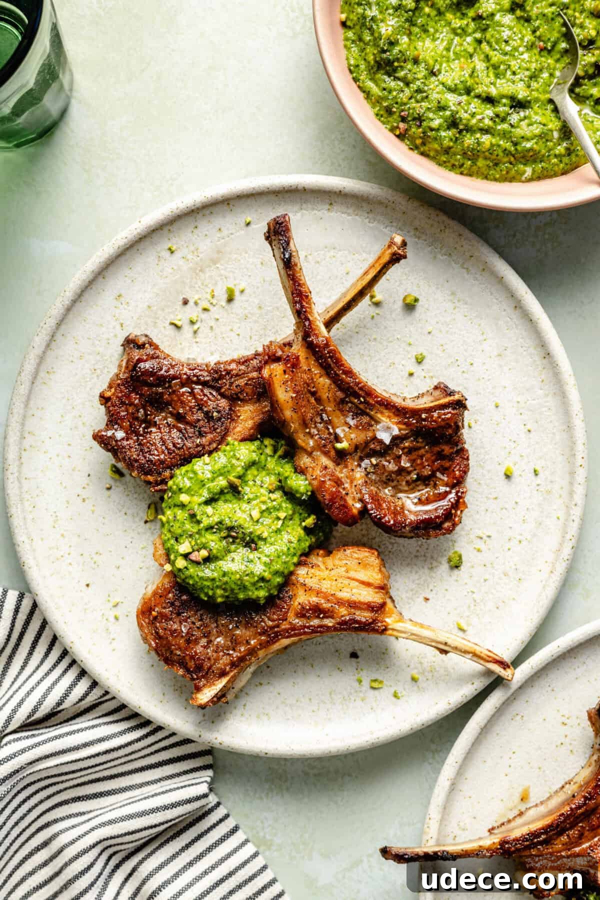 Grilled Lamb Chops with Fresh Arugula Pesto Recipe 5 a white plate with three lamb chops topped with a dollop of arugula-pistachio pesto