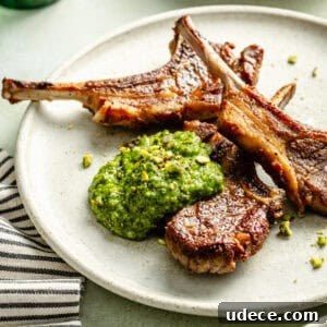 a plate of grilled lamb chops with a dollop of arugula-pistachio pesto and a striped napkin