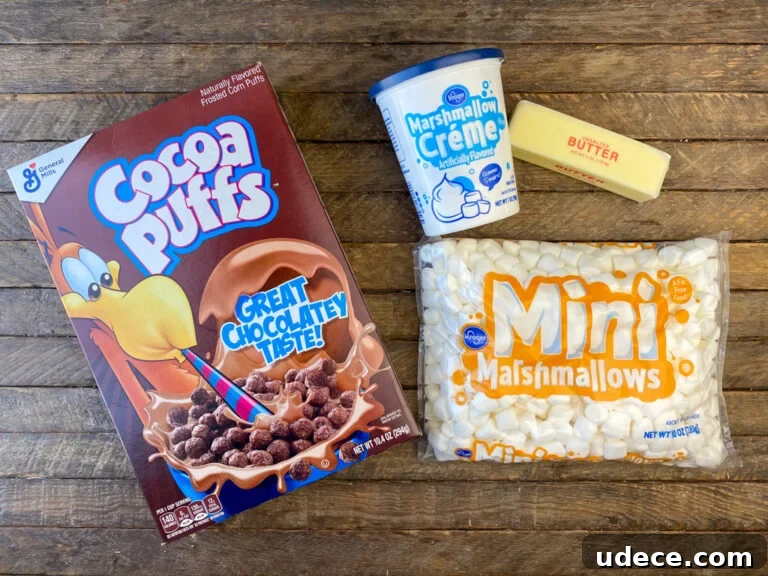 Homemade Cocoa Puffs Cereal Bars Recipe: Crispy Chocolate Treats 4 Ingredients to make cocoa puffs cereal bars are Box of Cocoa Puffs cereal, marshmallow creme, butter and mini marshmallows on a wooden counter top.