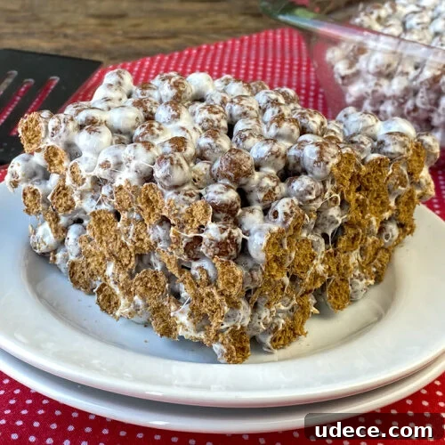 Crunchy balls of Cocoa Puffs cereal sliced open on the edges of a thick, sweet and sticky cocoa puffs treat on a white plate on a red napkin.