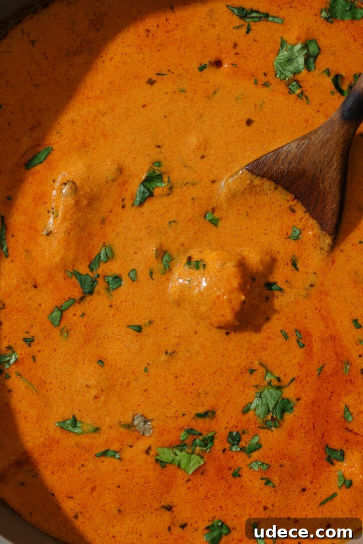 Authentic Butter Chicken Recipe: Tried and Perfected After 20 Tests 35 Close up of Butter Chicken in a skillet garnished with cilantro. with a wooden spoon.