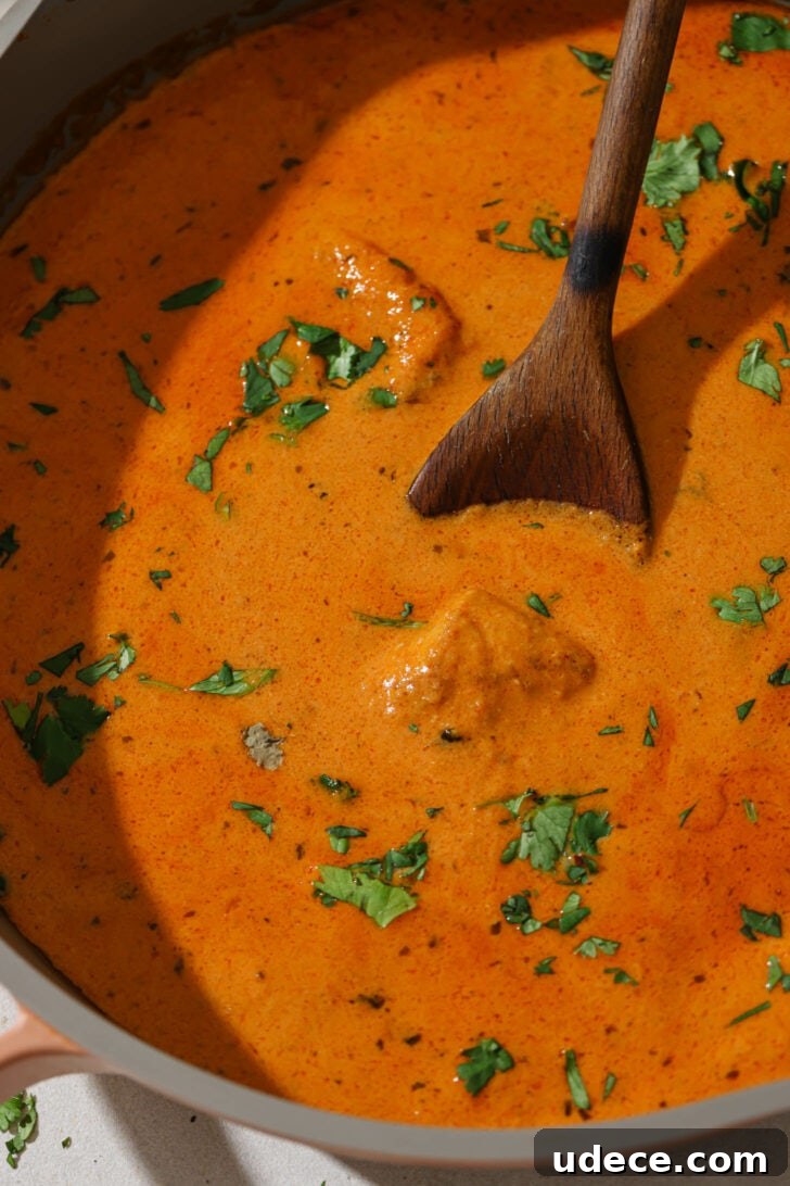 Authentic Butter Chicken Recipe: Tried and Perfected After 20 Tests 8 Close up of Butter Chicken in a skillet garnished with cilantro. with a wooden spoon.
