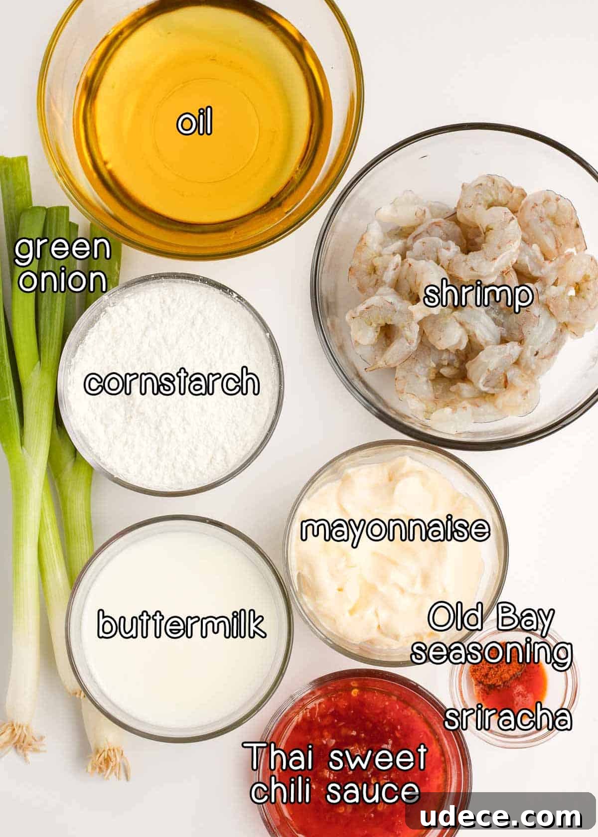 Overhead shot of ingredients - oil, green onion, cornstarch, shrimp, mayonnaise, buttermilk, Thai sweet chili sauce, old bay seasoning, and sriracha.