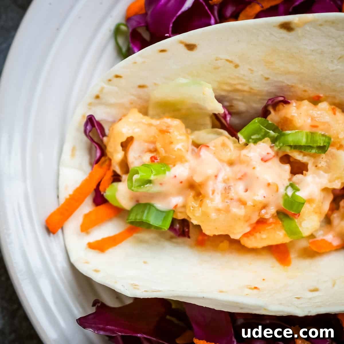 Overhead close up shot of a shrimp taco with shredded carrots and cabbage on a white plate.