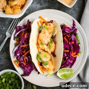 Overhead shot of one shrimp taco with shredded carrots and purple cabbage surrounding it and a lime wedge on the side of the white plate.
