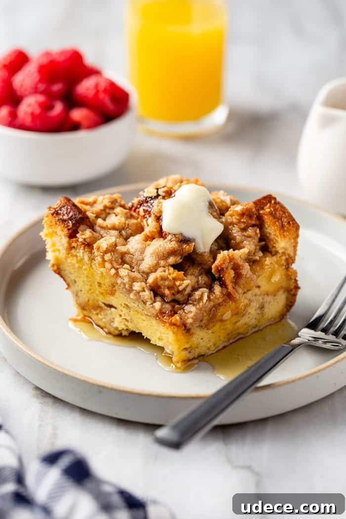 Overnight French Toast Casserole Recipe for Make-Ahead Brunch 2 Slice of french toast casserole topped with butter and syrup next to a fork on a white plate. a bowl of raspberries and a glass of orange juice are in the background.