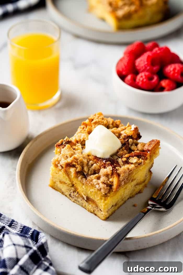 Overnight French Toast Casserole Recipe for Make-Ahead Brunch 12 Slice of overnight french toast casserole topped with butter next to a fork on a white plate. Orange juice and fresh raspberries are in the background