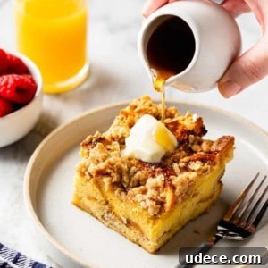 Overnight French Toast Casserole Recipe for Make-Ahead Brunch 14 Hand drizzling maple syrup over a slice of buttered overnight french toast casserole on a white plate. A glass of orange juice is in the background