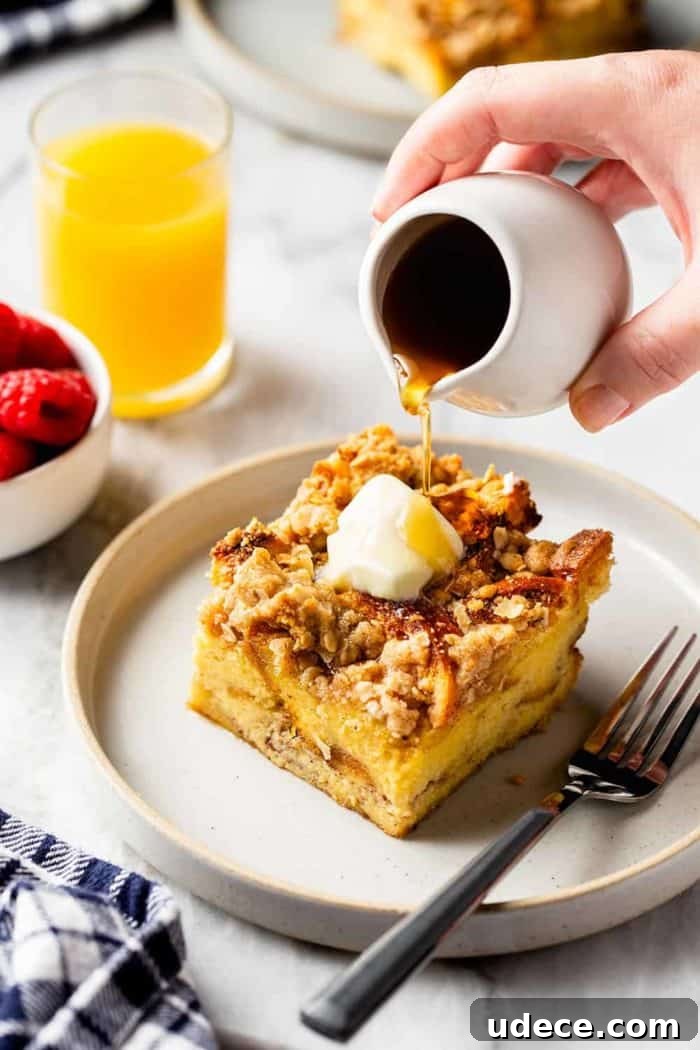 Overnight French Toast Casserole Recipe for Make-Ahead Brunch 8 Hand drizzling maple syrup over a slice of buttered overnight french toast casserole on a white plate. A glass of orange juice is in the background