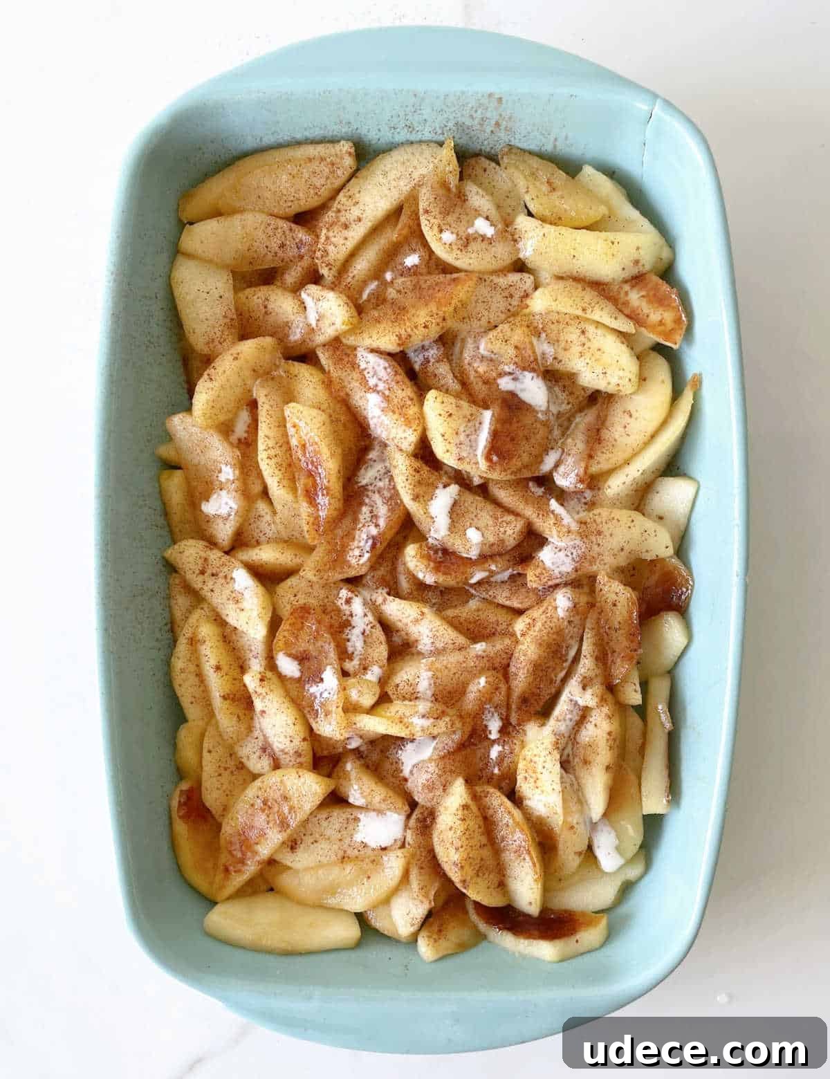 Caramel Apple Dump Cake Recipe — Quick Crowd-Pleasing Dessert 11 Top view of blue ceramic dish with cooked cinnamon apples on white surface.