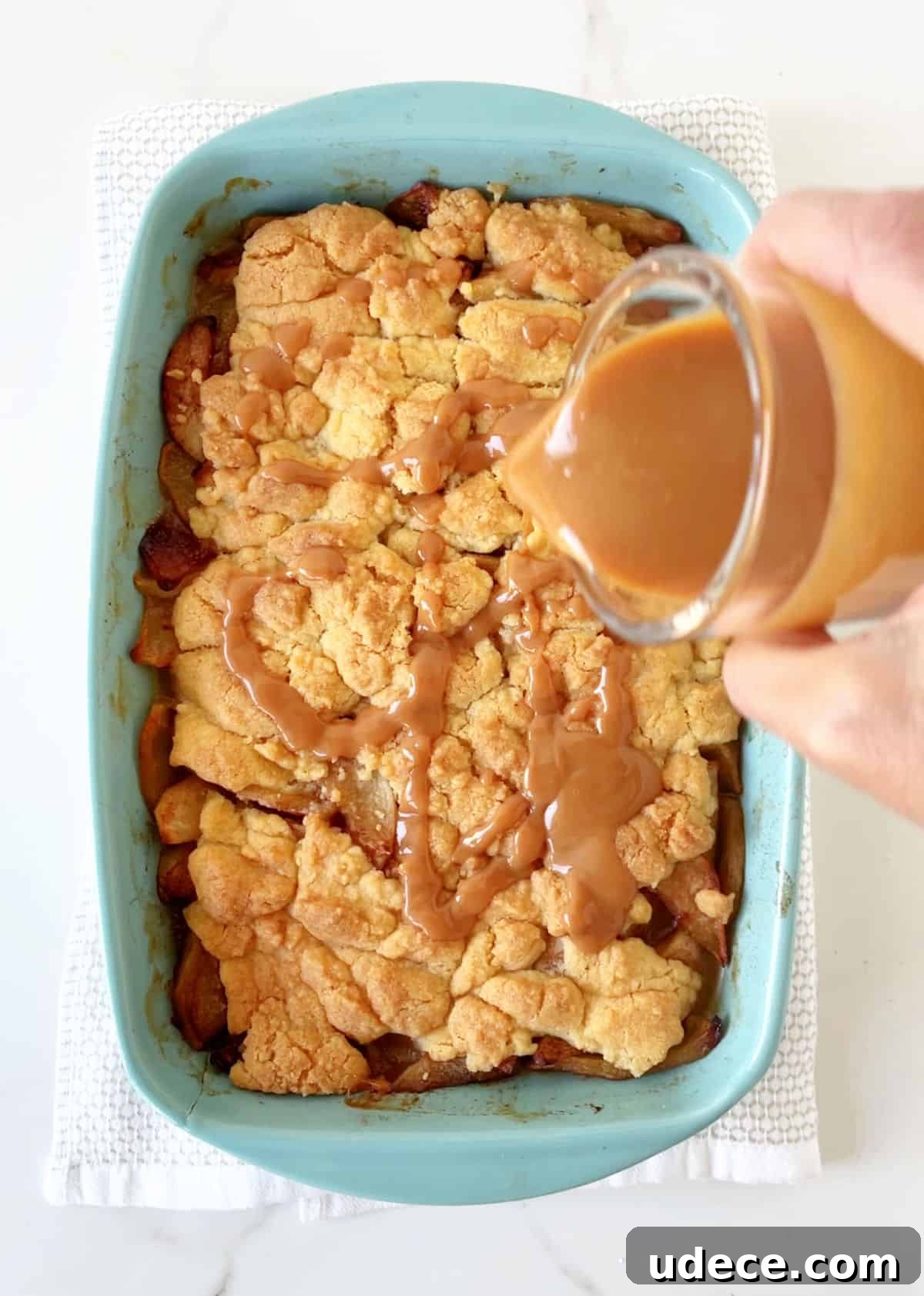 Caramel Apple Dump Cake Recipe — Quick Crowd-Pleasing Dessert 12 Drizzling caramel over baked dump cake in blue dish on towel over white marble surface