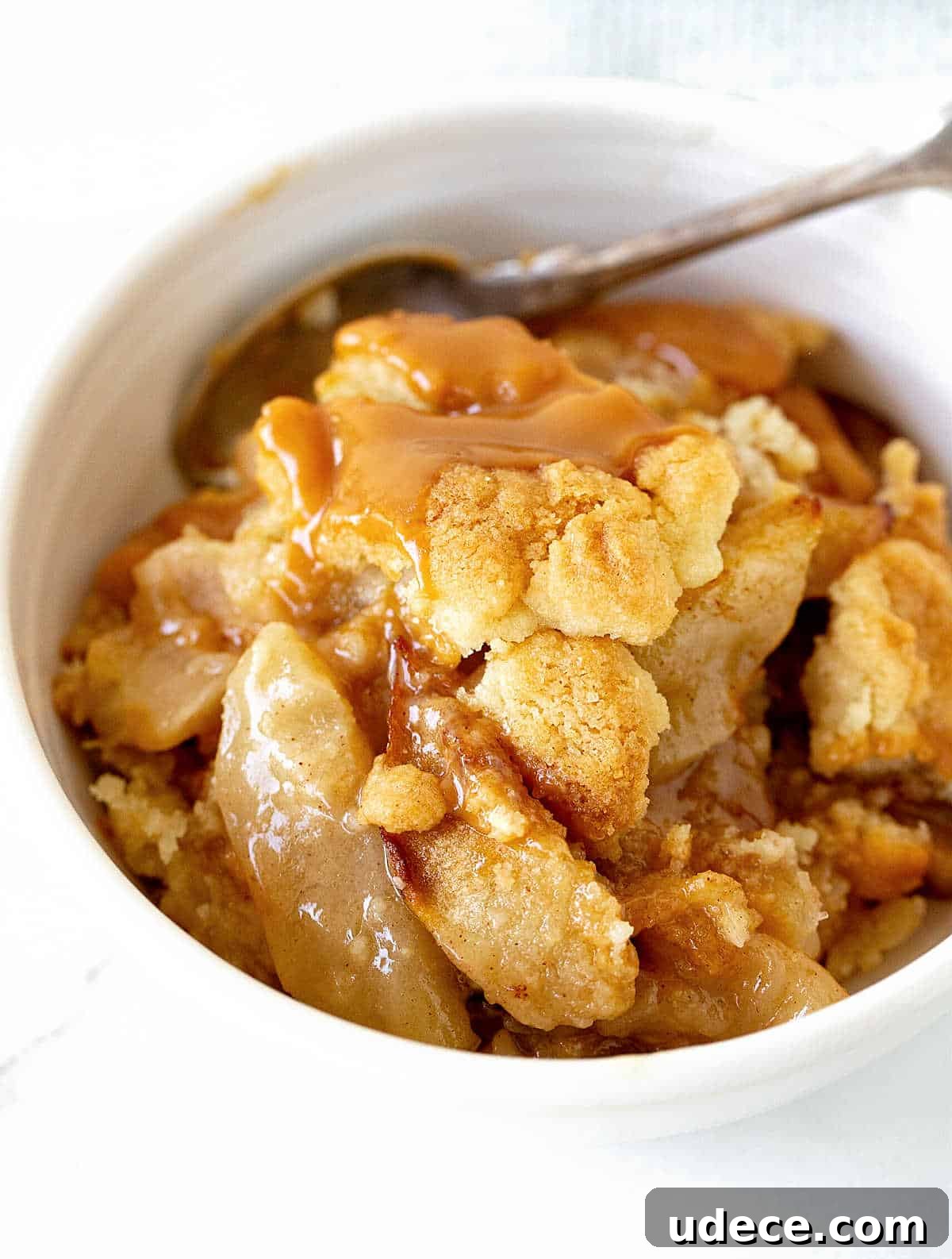 Caramel Apple Dump Cake Recipe — Quick Crowd-Pleasing Dessert 13 Serving of apple dump cake in white bowl with silver spoon, white surface