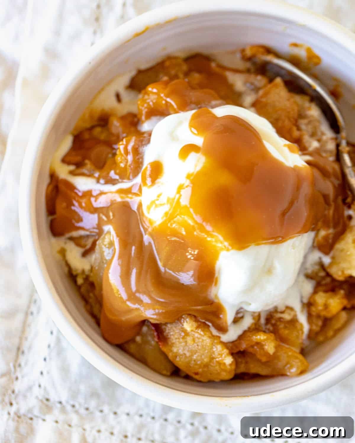 Caramel Apple Dump Cake Recipe — Quick Crowd-Pleasing Dessert 3 Caramel topped ice cream scoop over apple dump cake in white bowl, white napkin.