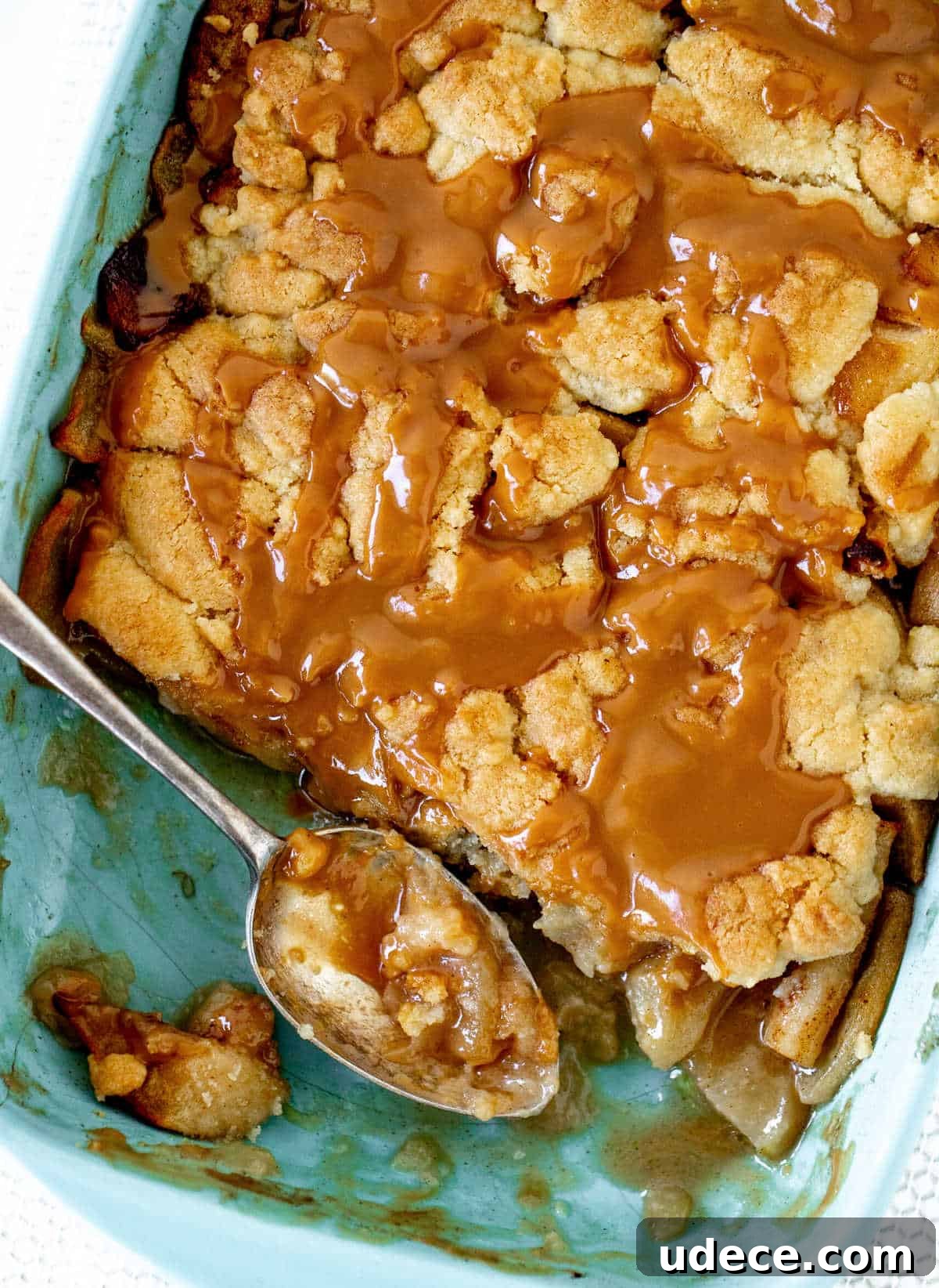 Caramel Apple Dump Cake Recipe — Quick Crowd-Pleasing Dessert 4 Blue ceramic dish with apple caramel dump cake, silver serving spoon, white surface