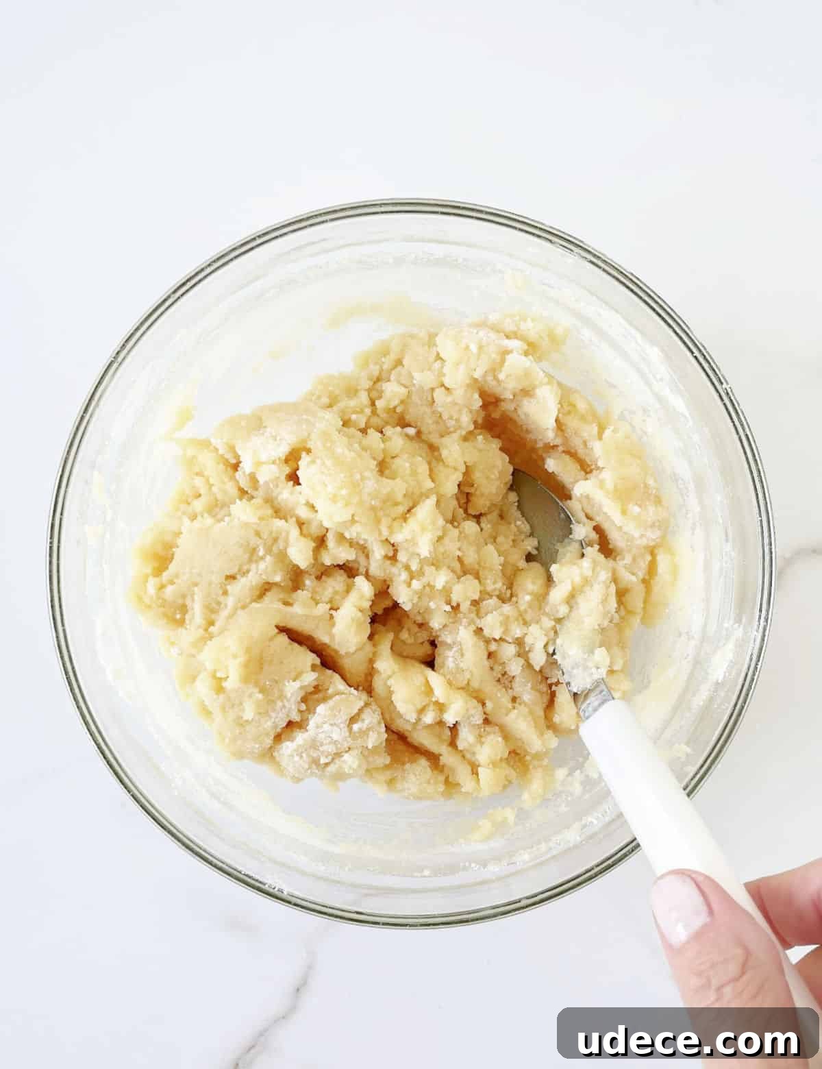 Caramel Apple Dump Cake Recipe — Quick Crowd-Pleasing Dessert 7 Cake mix and butter topping mixture in a glass bowl. A white spoon. White marble surface.