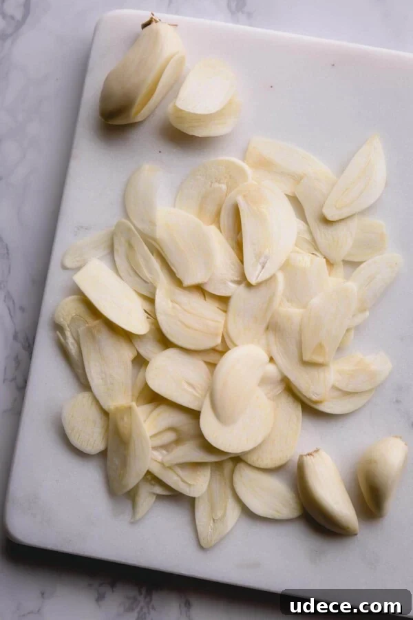 Crispy Garlic Chips Recipe: Homemade Thin Garlic Crisps 3 thinly sliced garlic cloves on a white marble cutting board.