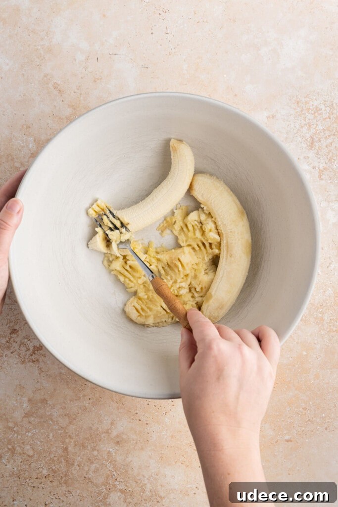 Smashing 3 ripened bananas with a fork.