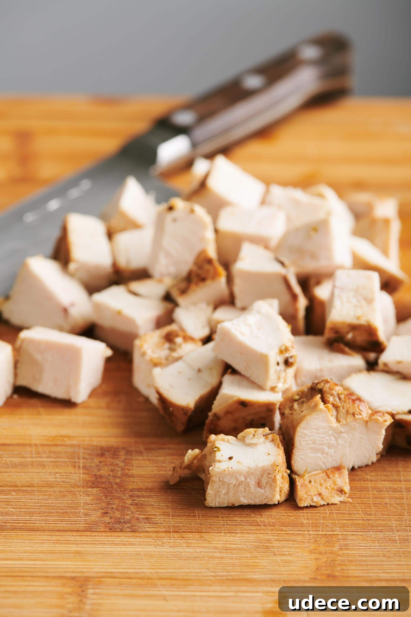 How to Cube Chicken Breast for Evenly Cut Pieces 2 Cubed cooked chicken breast on a cutting board with a knife.