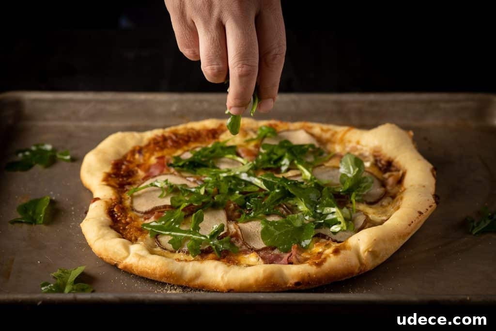 Dutch Oven Pizza with Pear, Brie & Prosciutto Recipe 4 Arugula being sprinkled on top of a Dutch oven pizza.