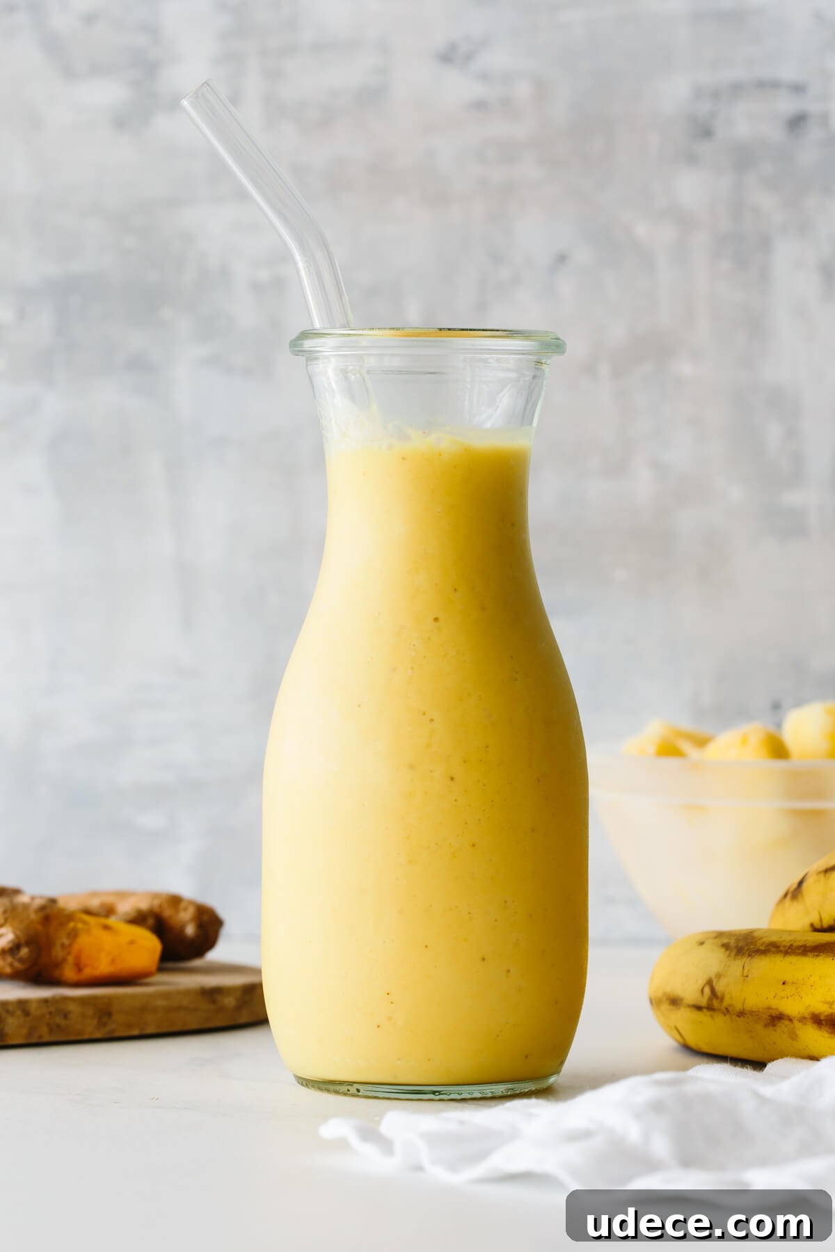 Turmeric smoothie in a glass jar with straw and ingredients in the background.