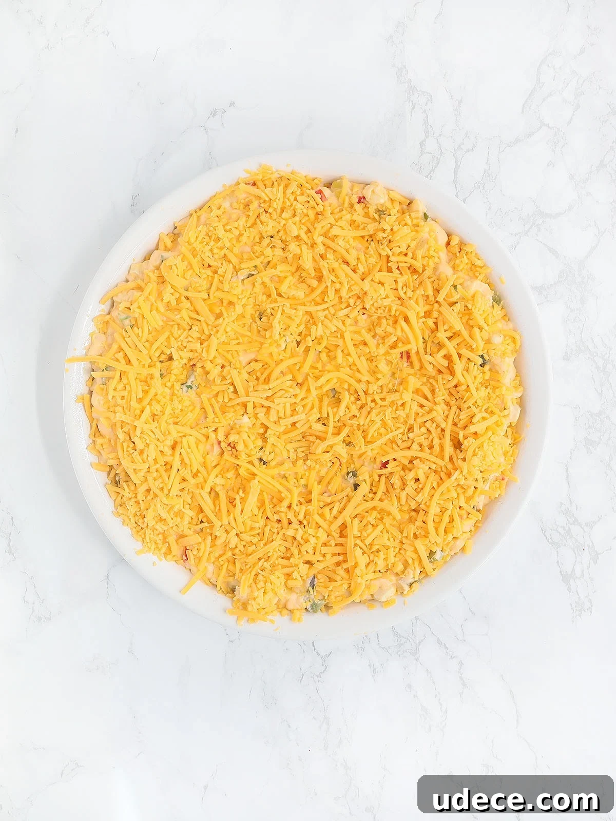 corn dip topped with shredded cheese before it has been baked in the oven